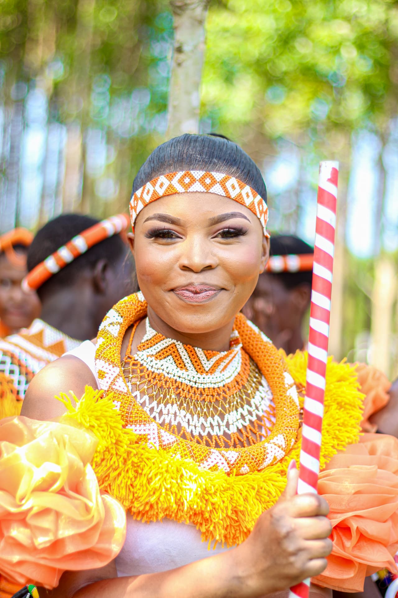 Smiling portrait of a woman in layered Zulu beadwork holding a ceremonial staff