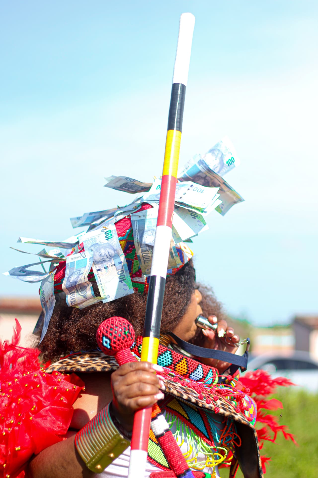 Celebrant in beaded regalia and money-adorned headpiece blowing a whistle during a ceremony