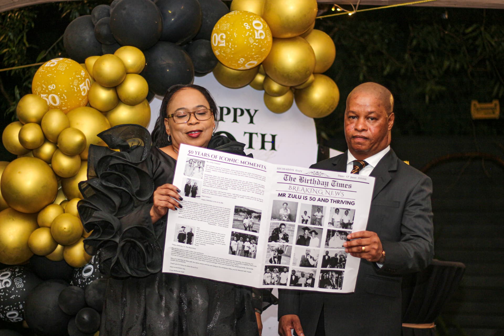 Couple holding a custom newspaper tribute at a black and gold 50th birthday celebration