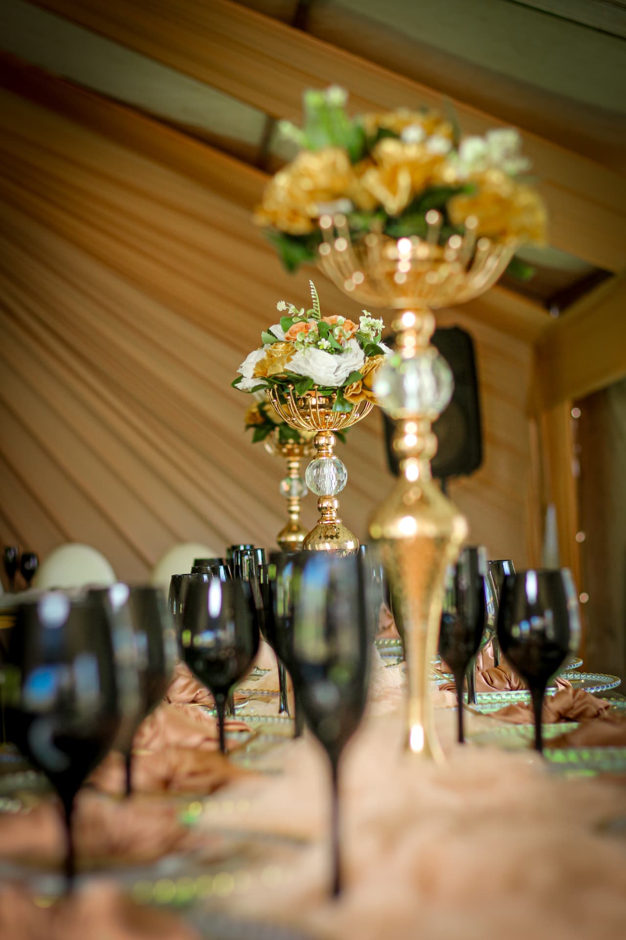 Gold floral centrepieces rising above black glassware at a styled reception table