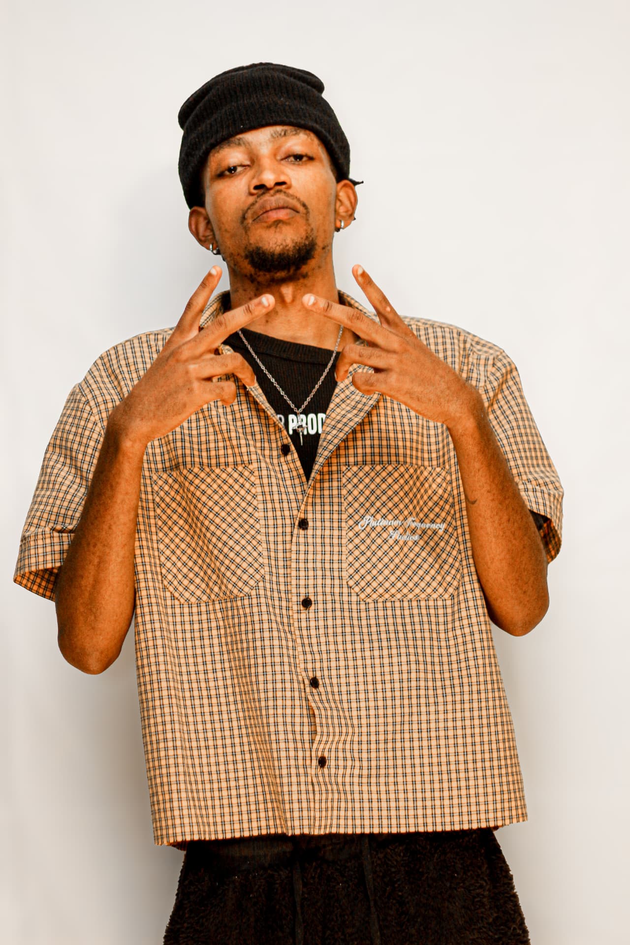 Studio portrait of a young man in a checked shirt and beanie throwing hand signs